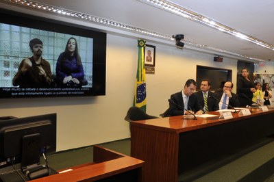 À esquerda, imagem do vídeo apresentado na Mesa de Abertura da Terceira-Secretária da Câmara dos Deputados, Deputada Mara Gabrilli. Na Mesa de abertura do Seminário, da esquerda para a direita: Sr. Sérgio Paulo Da Silveira Nascimento, Diretor do Departamento de Políticas Temáticas dos Direitos da Pessoa com Deficiência; Deputado Aelton Freitas, Presidente da Comissão de Defesa dos Direitos das Pessoas com Deficiência; e Sr. Dario Rais Lopes, Secretário Nacional de Transporte e da Mobilidade Urbana do Ministério das Cidades.